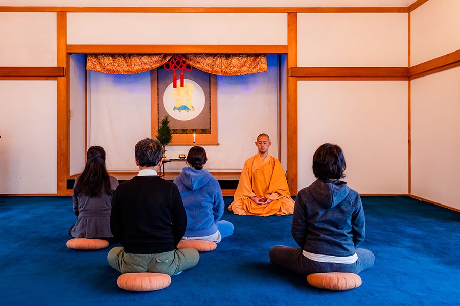 People sitting on cushions in front of a praying monk in Ekoin Temple