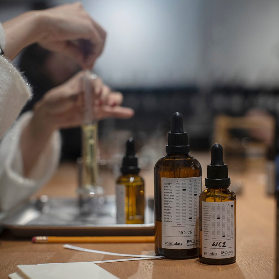 A person making a fragrance, with brown glass bottles and test tubes on a table. 