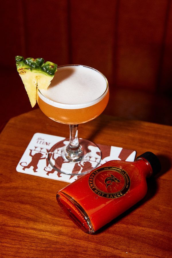 A bottle of Flagrant Sauce next to a cocktail with a slice of pineapple on top.   (pls pick 2 images)  