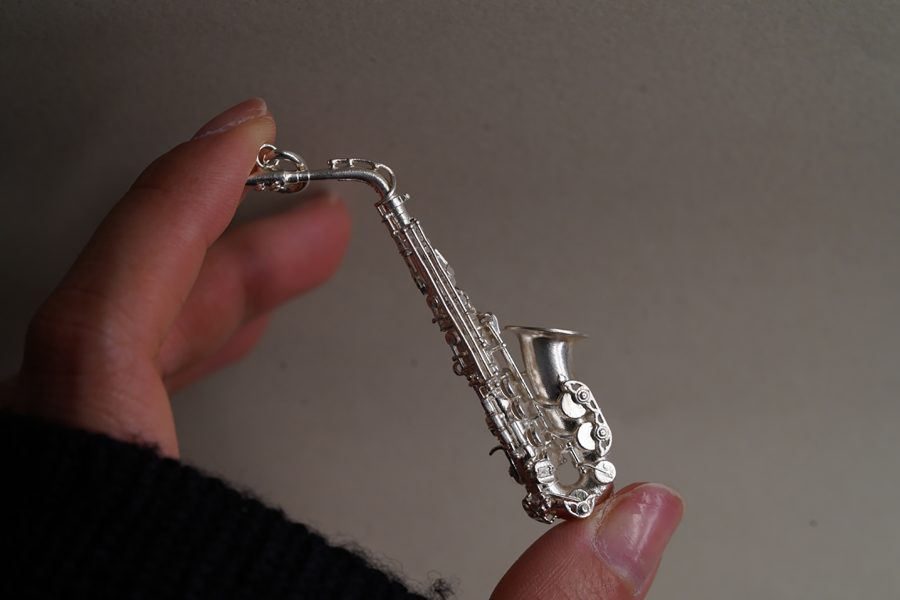 A hand holding a miniature silver saxophone.