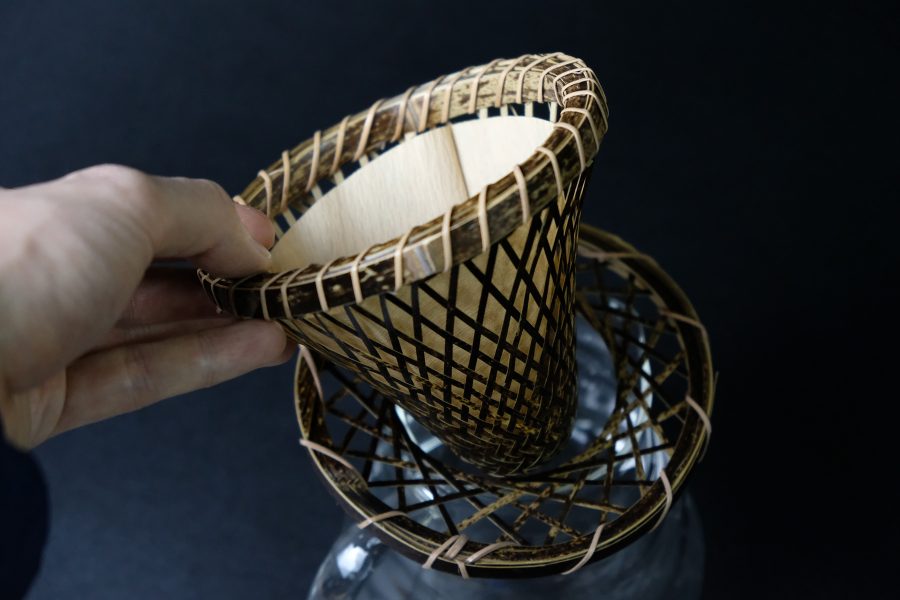 A hand holding a wicker cone over a glass container. 