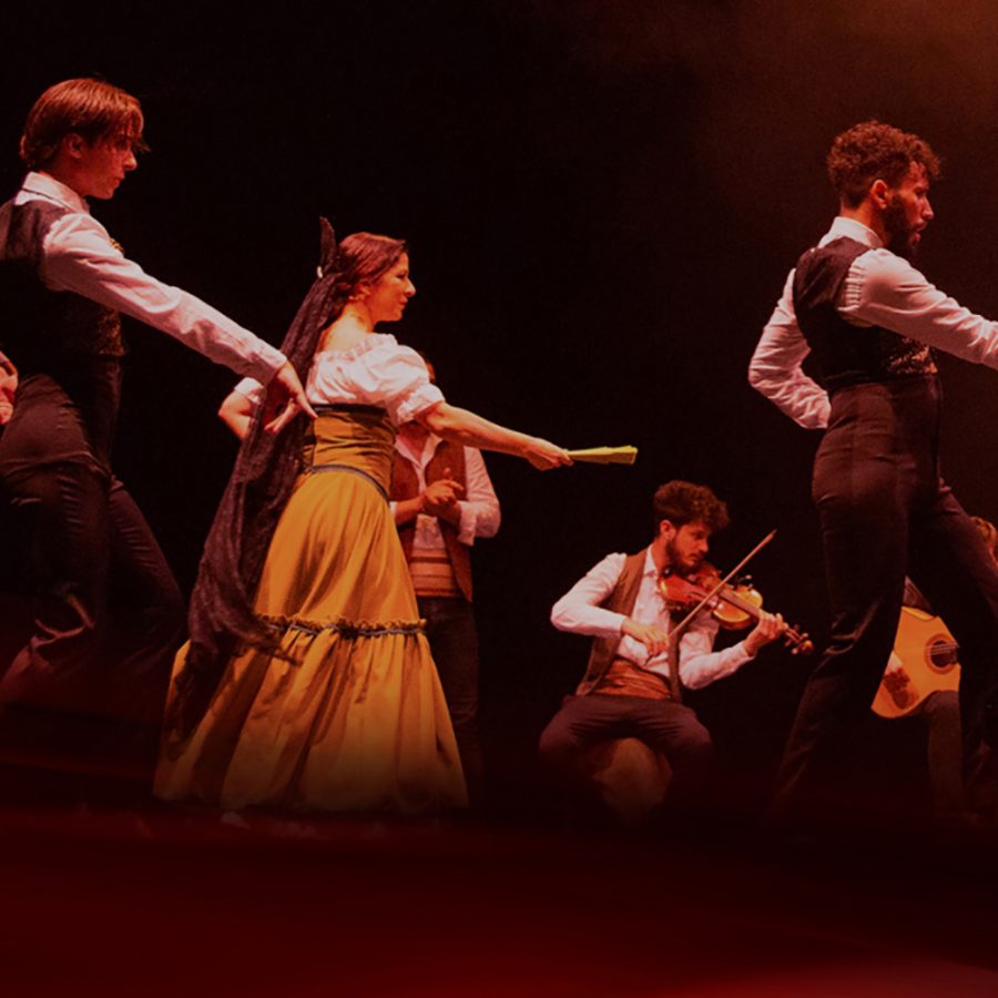 Three dancers pose on a stage while musicians play behind them, during a performance of Carmen. 