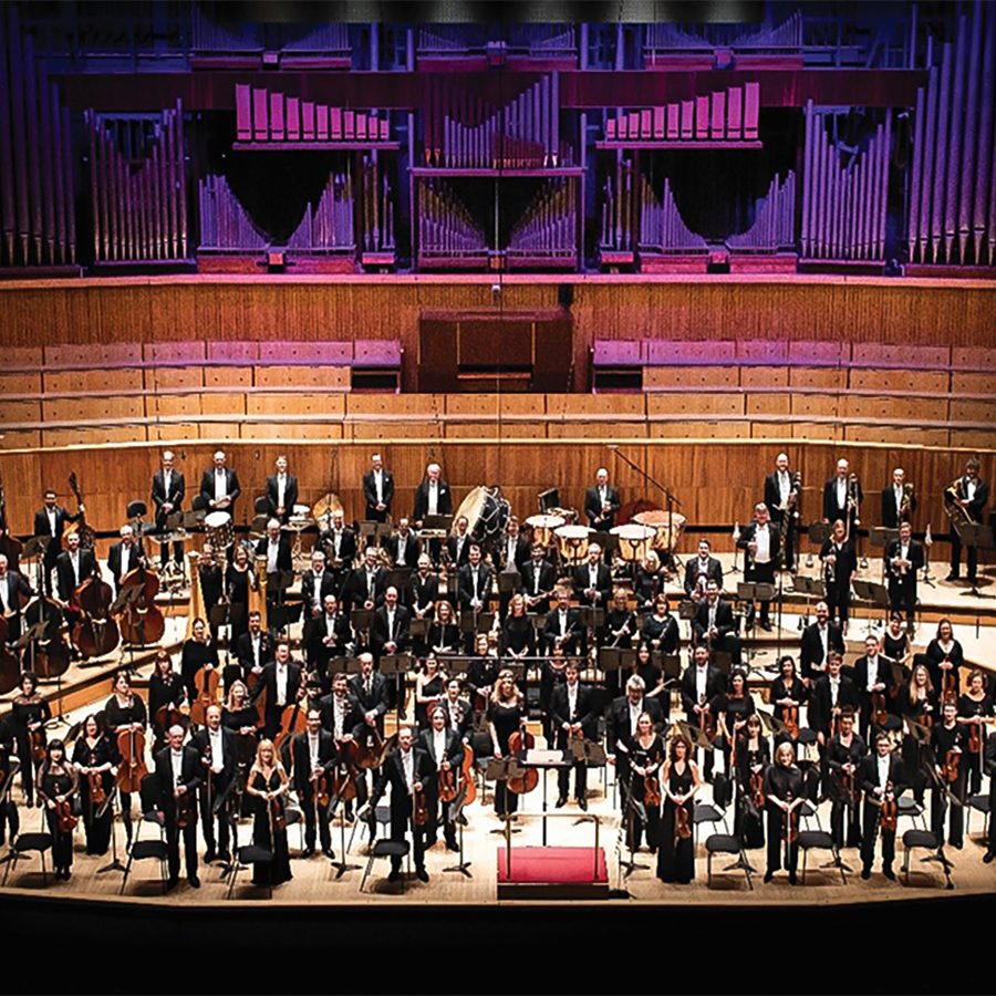 Orchestra musicians stand on a large stage. 