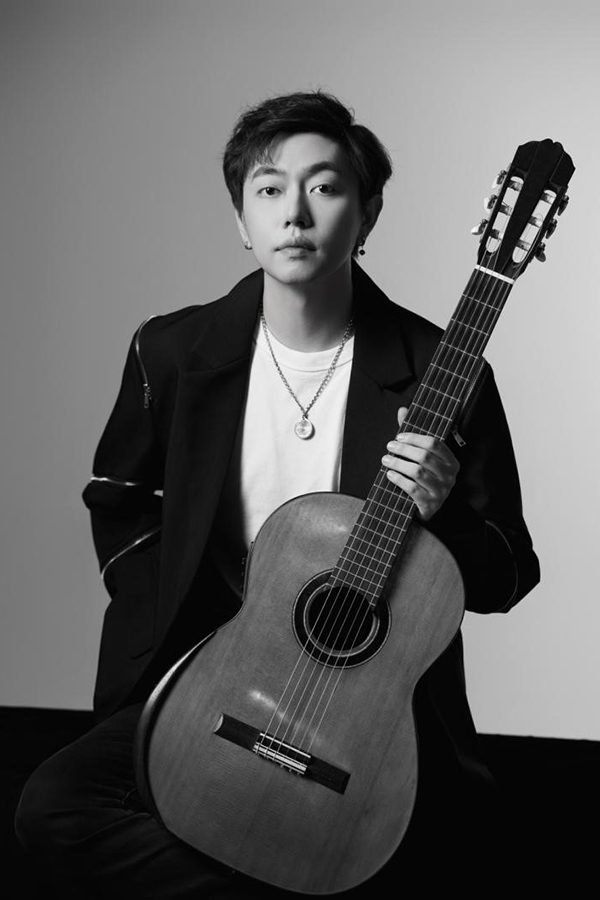 Classical guitarist Pu Xiaobo holds his guitar, in black and white.  