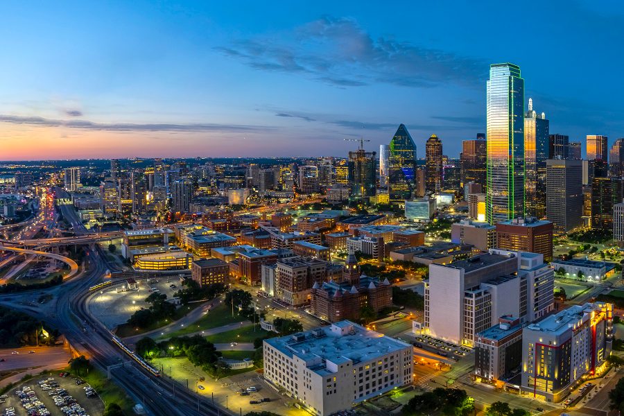 Dallas’s skyline in the evening, its skyscrapers reflecting the setting sun and the roads lit up by vehicles.