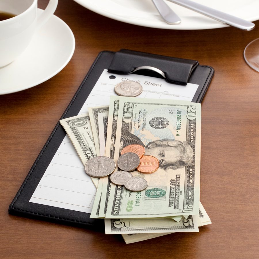 American dollar bills and coins sit atop a receipt at a restaurant when it’s time to pay the bill and a tip.