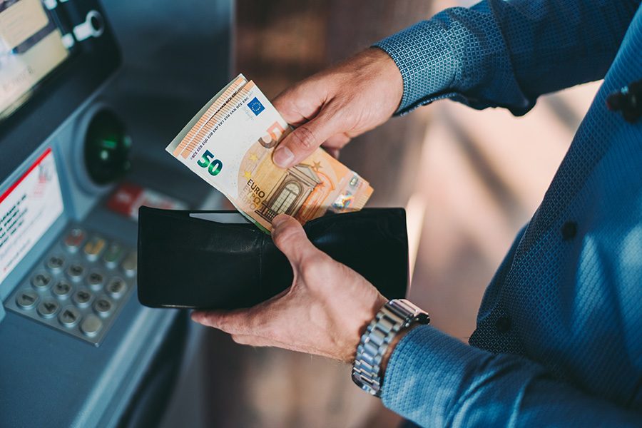 A person withdraws cash from the ATM and stores it in their wallet in advance of shopping in Munich, which has many cash-only stores. 