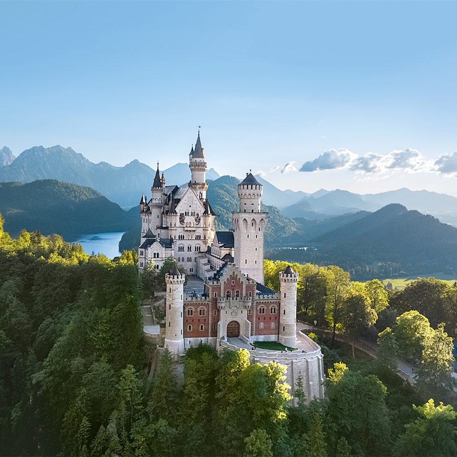 Neuschwanstein Castle, a beautiful day trip from Munich, stands tall against lush green mountains on a sunny day.