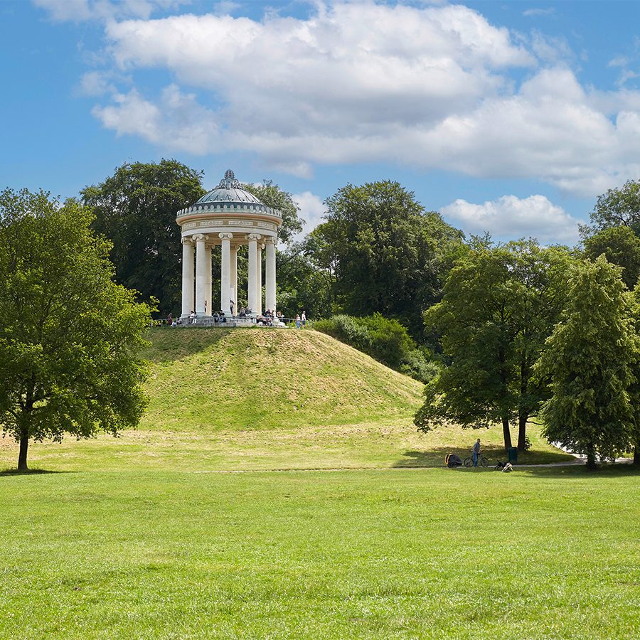 The Monopteros sits atop a grassy hill in The English Garden, Munich on a sunny day.  