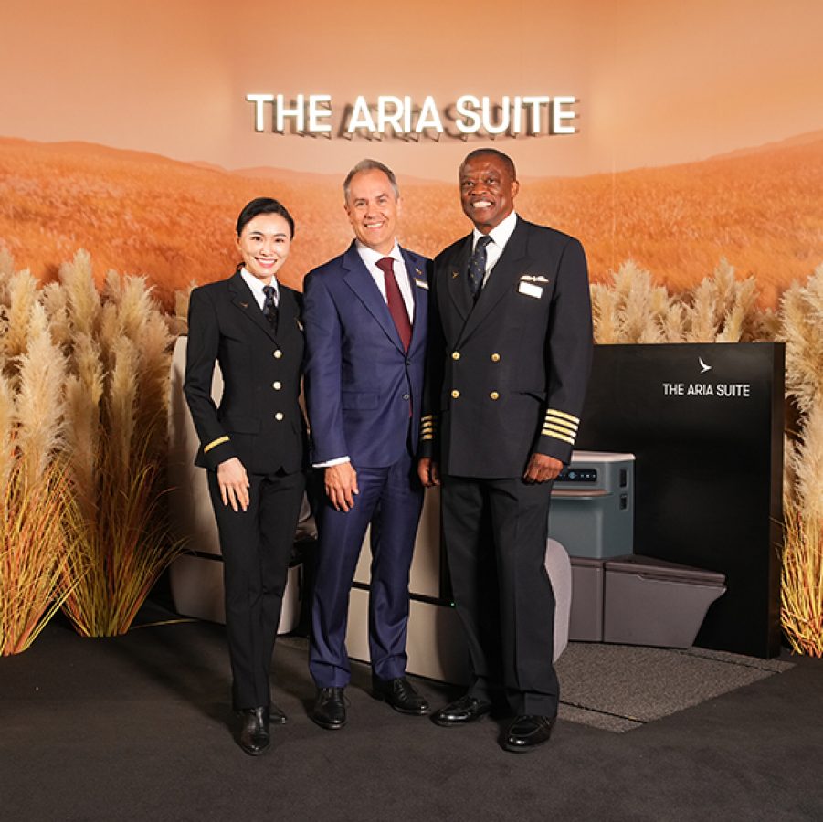 Two pilots, one male and one female, standing on either side of Cathay Chief Operations and Service Delivery Officer Alex McGowan in front of the Aria Suite display at The Diamond Drinks in Hong Kong.