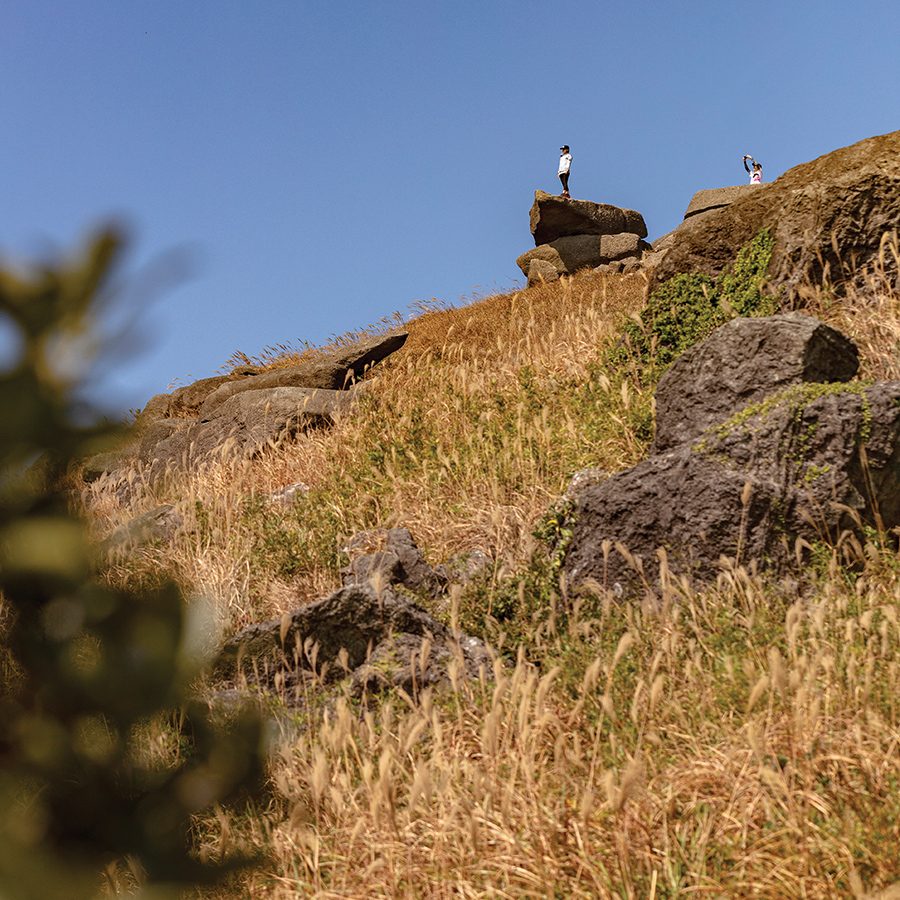 A wild mountain landscape with someone standing on top of a rock in the distance.