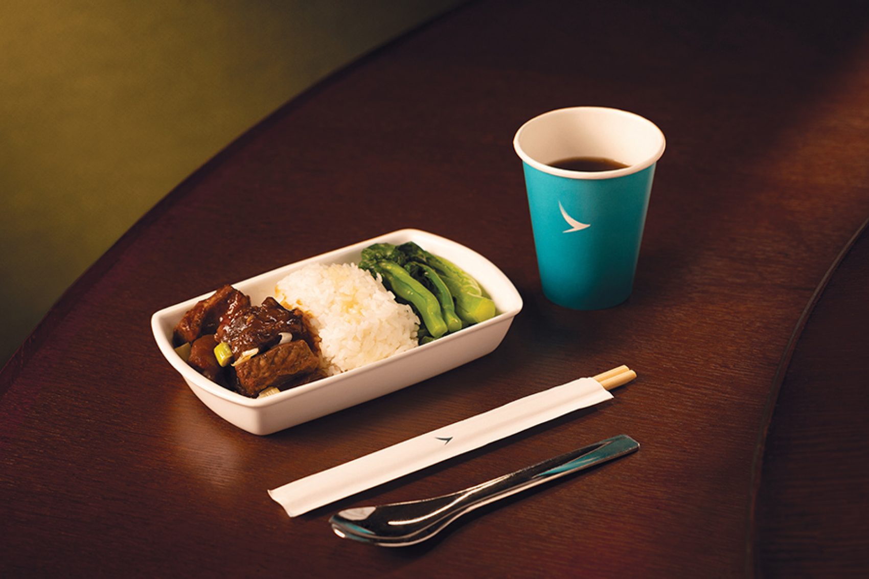 A white dish of Michelin-starred Yat Tung Heen in-flight meal braised duck with plum sauce and taro with a blue Cathay cup and utensils served in Cathay Pacific’s Premium Economy and Economy cabins.