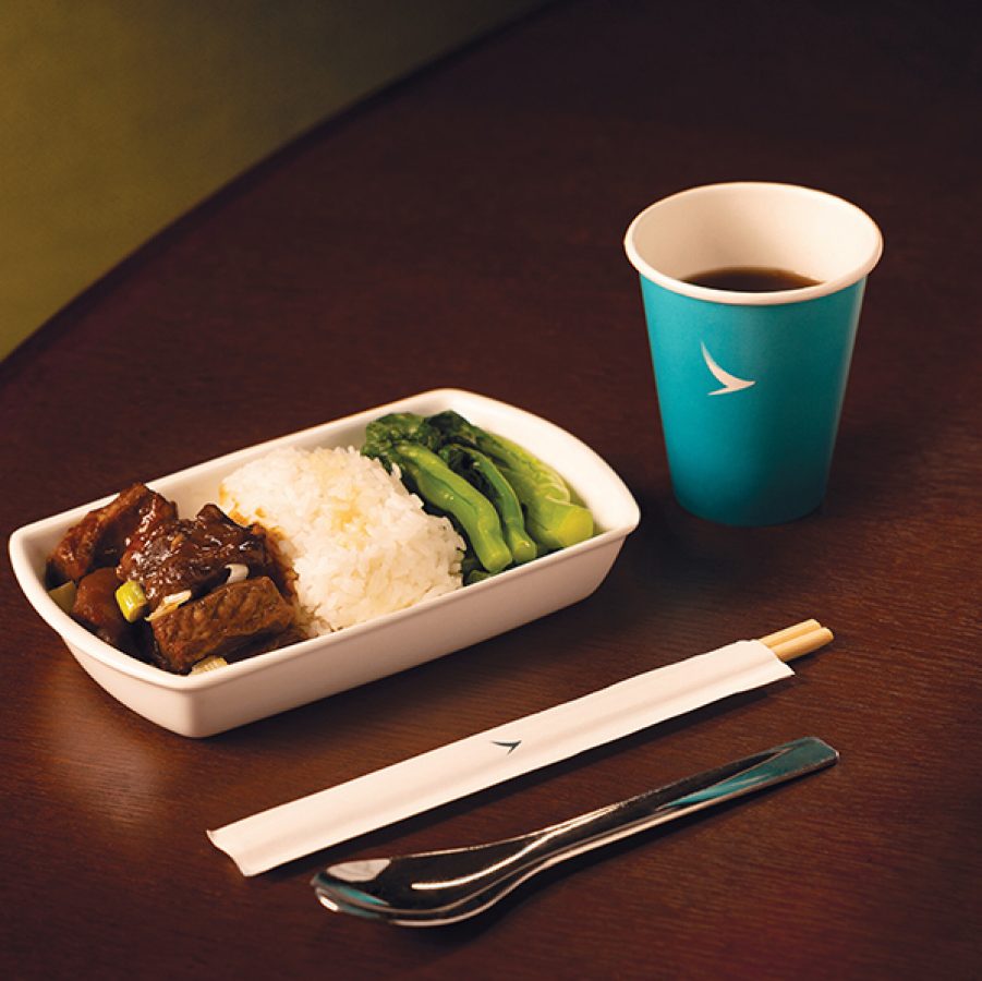 A white dish of Michelin-starred Yat Tung Heen in-flight meal braised duck with plum sauce and taro with a blue Cathay cup and utensils served in Cathay Pacific’s Premium Economy and Economy cabins.
