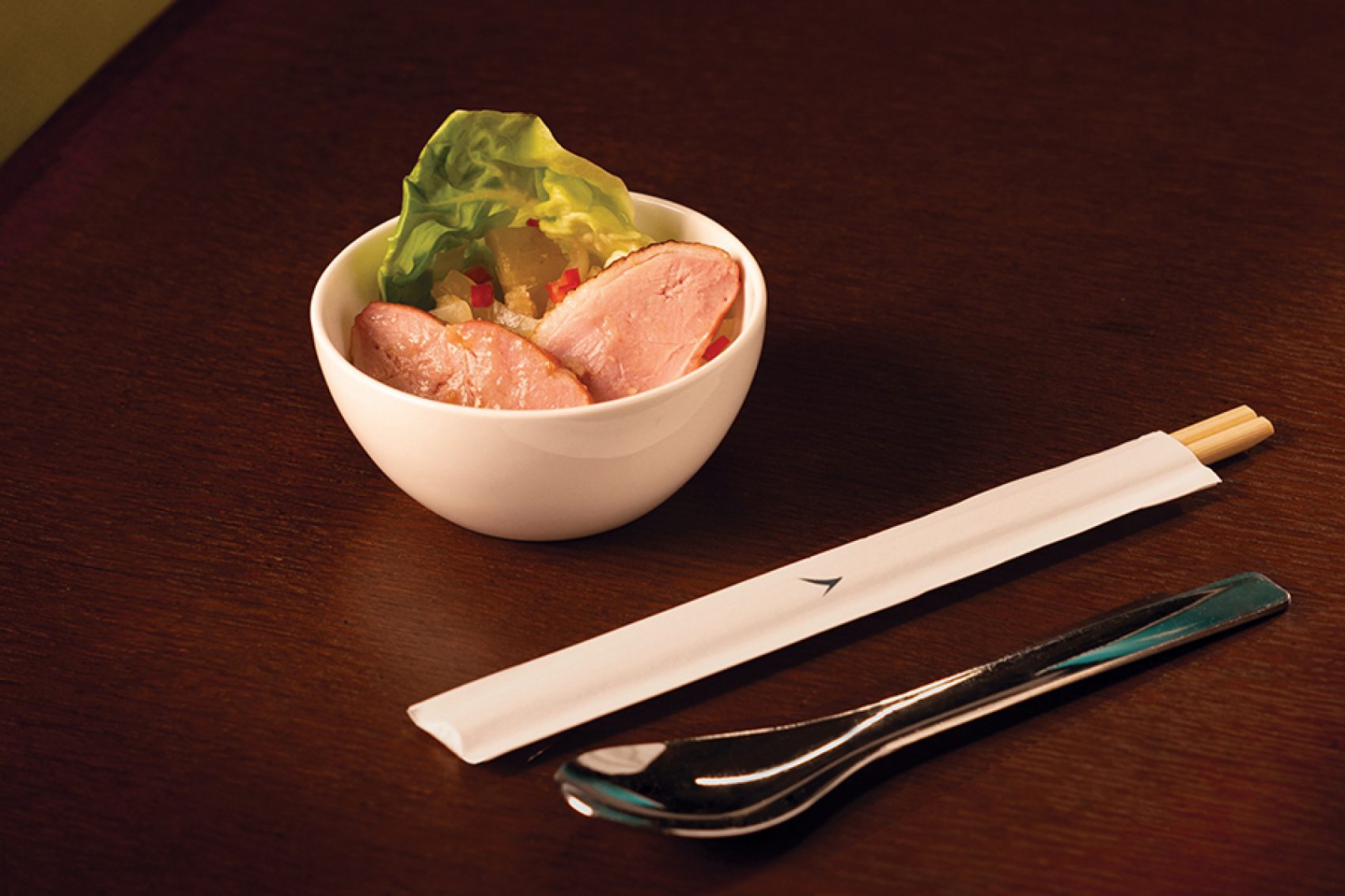 A white bowl of Michelin-starred Yat Tung Heen in-flight meal smoked duck breast with Cathay utensils served in Cathay Pacific’s Premium Economy and Economy cabins. 