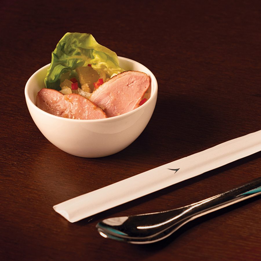 A white bowl of Michelin-starred Yat Tung Heen in-flight meal smoked duck breast with Cathay utensils served in Cathay Pacific’s Premium Economy and Economy cabins. 