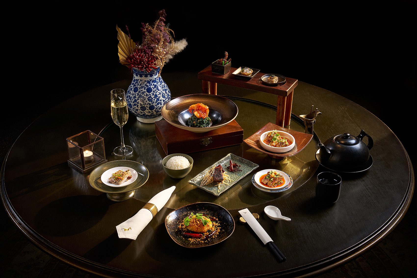 A table laden with dishes by Hong Kong’s Mott 32 for Cathay along with a vase, a teapot and a glass of champagne.