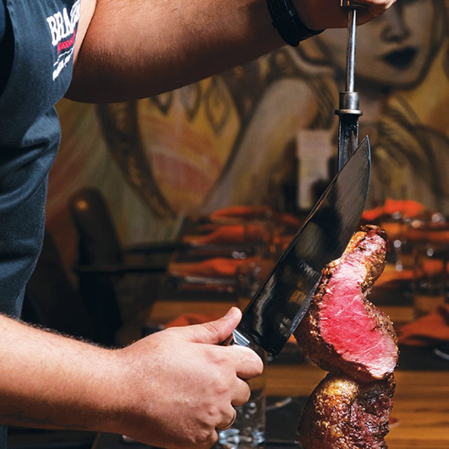 A close-up of a man carving a piece of steak on a wooden cutting board, served at Braza Churrascria, Hong Kong.