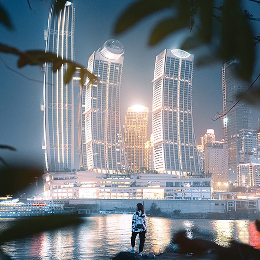 A night view of a person looking out across the sea towards Raffles City and Chongqing skyline.