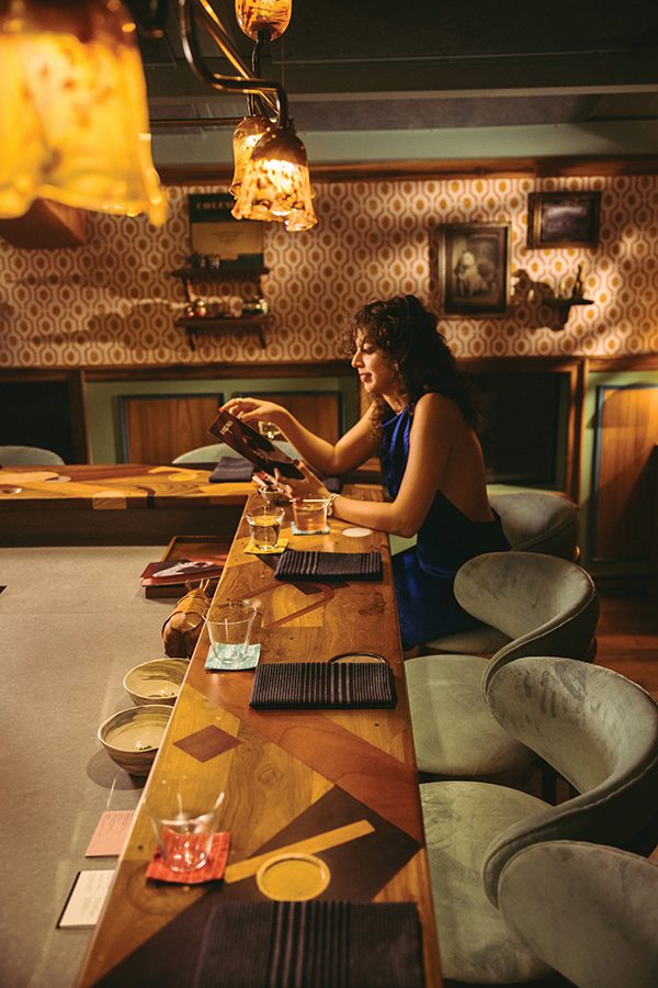 A view inside Papa’s restaurant in view, featuring modern interior design, decor and a woman sitting at the bar and smiling while looking at the menu.