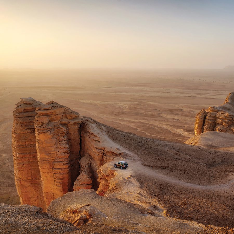 A bird’s eye view of a van parked at Edge of the World cliff side desert landscape in Riyadh during sunset.