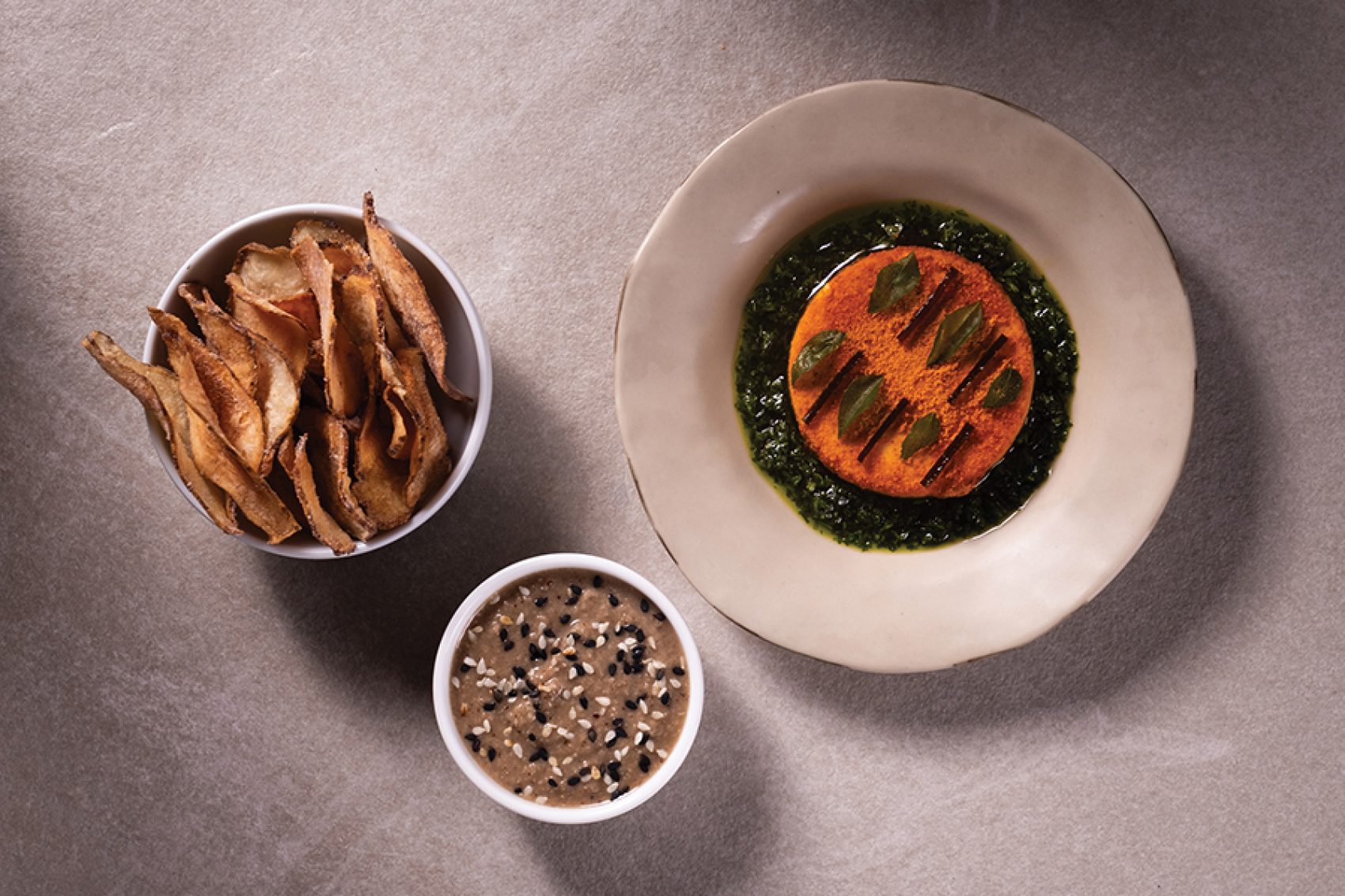 A flat lay of three dishes, masque podi cashew, curry leaf, and sunchoke chips served in fine dining Masque in Mumbai