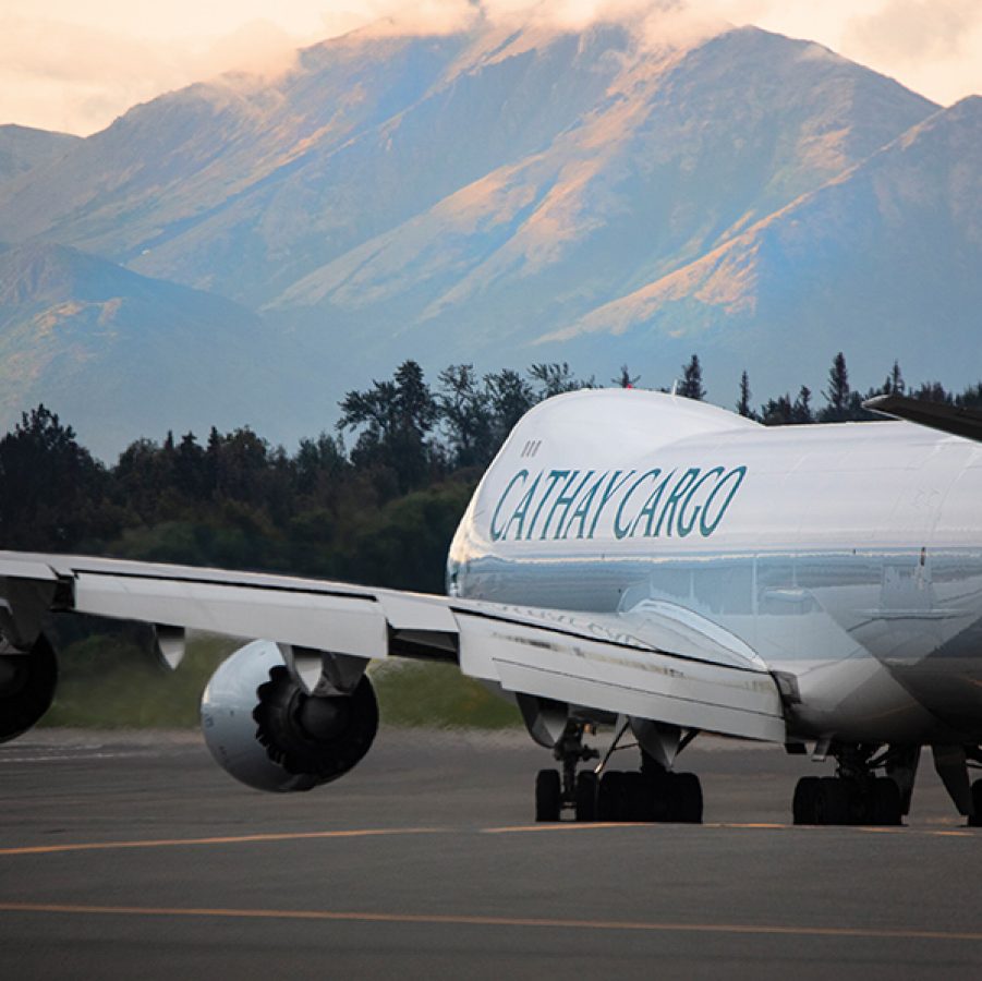 A view of a Cathay Cargo aircraft from the back getting ready to take off during daytime, and a view of mountains from a distance.