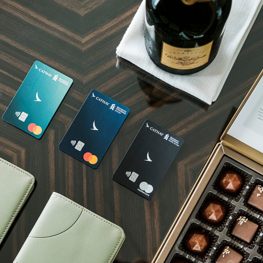 The different Standard Chartered Cathay Mastercards arranged across a table alongside passport holders, chocolates and a bottle of wine.