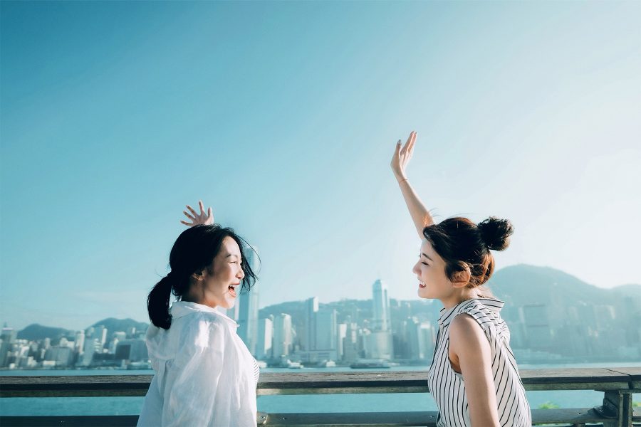 Two women stood at a harbour smiling at each other with their hands in the air.
