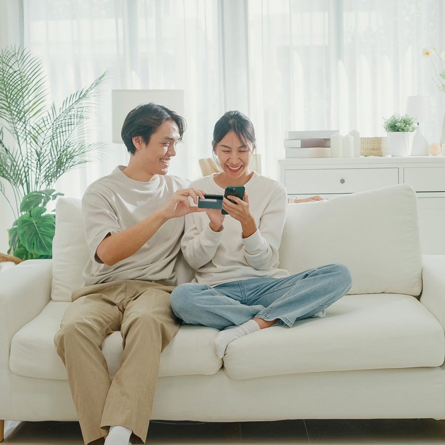 A woman and a man smile as they enter their credit card details into a phone while online shopping.  