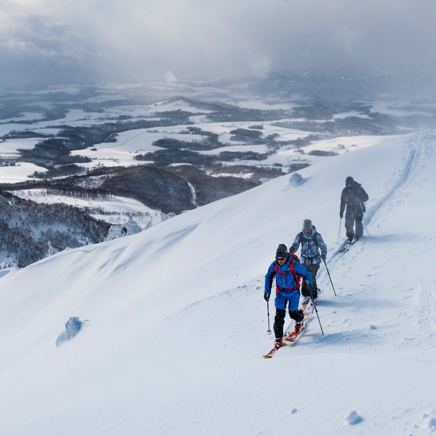 Three people skiing down the snowy mountains on a cloudy day at Niseko