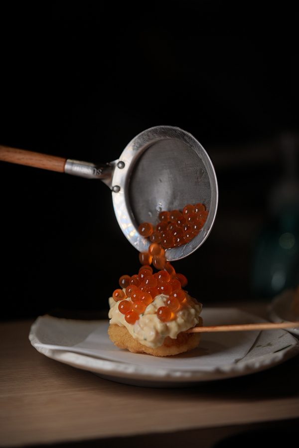 A close-up of someone pouring a ladle of salmon roe over a dish served at Inoshishi in Hong Kong.