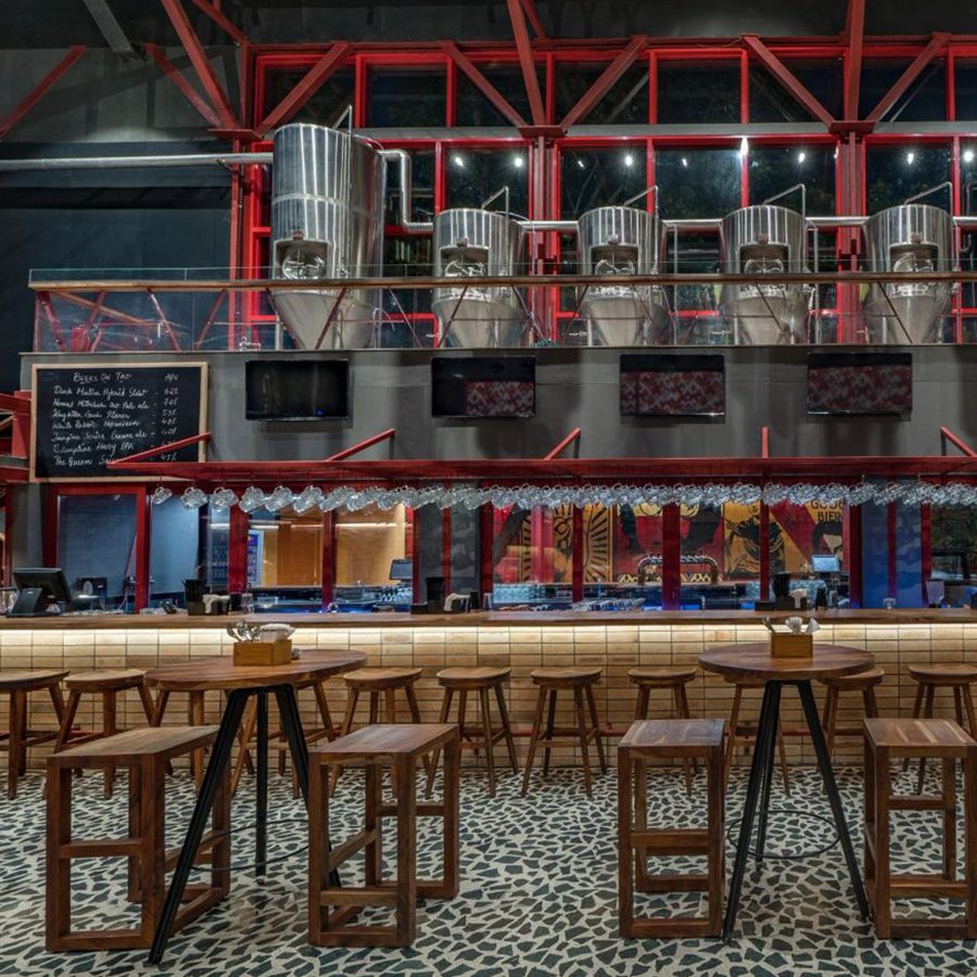 A view of the expansive and rustic interiors at Broadway Brewery in Hyderabad, featuring wood beams, stacked firewood and wooden table and seating 