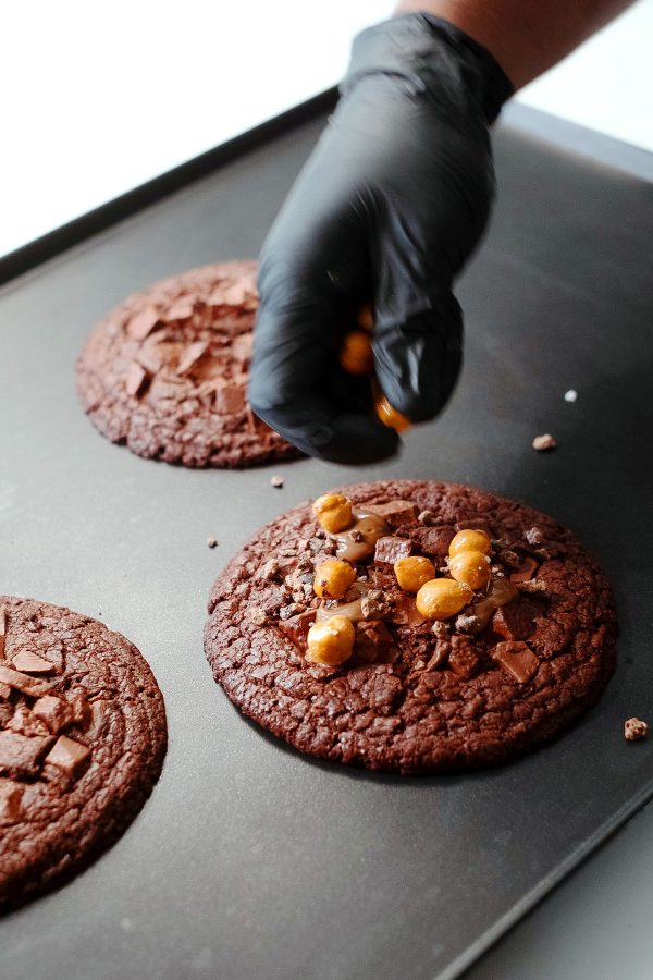 A close-up of a person sprinkling ingredients onto a chocolate cookie, served at Manam Chocolate Karkhana café in Hyderabad