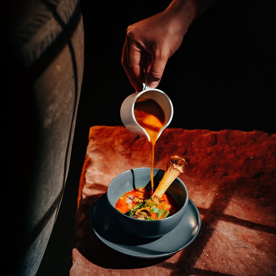 A close-up of a person pouring country chicken soup into a bowl with chicken bone and vegetables, served at Terrai Neo-telangana kitchen and bar in Hyderabad 