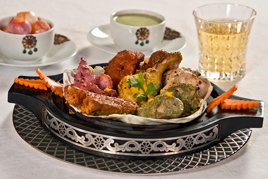 A close-up of a meat platter served on a hot place with chai and dessert at Jewel of Nizam – The Minar in Hyderabad