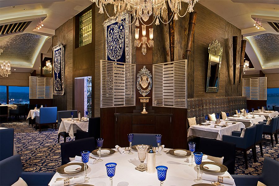 An interior view of a large, round dining table at Jewel of Nizam – the Minar in Hyderabad, with a view of the sunset and lush greenery from a distance 