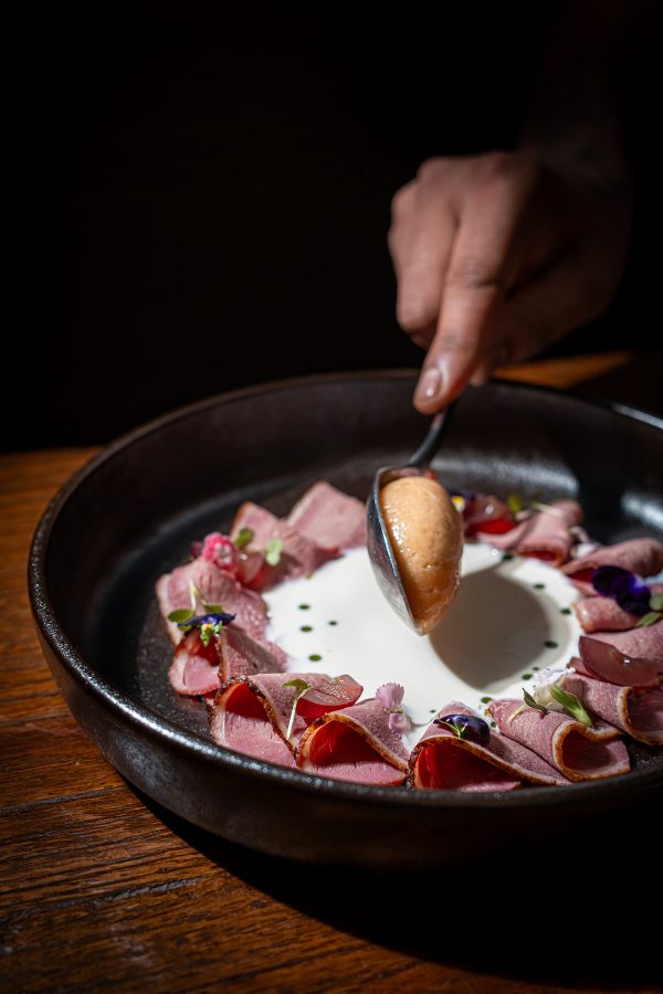 A hand spoons puree onto a dish with slices of smoked duck at Boca, Dubai. 