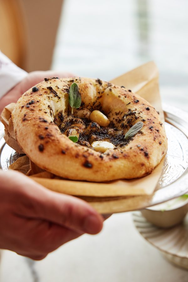Hands holding out a plate with fresh flatbread at Sufret Maryam, Dubai.