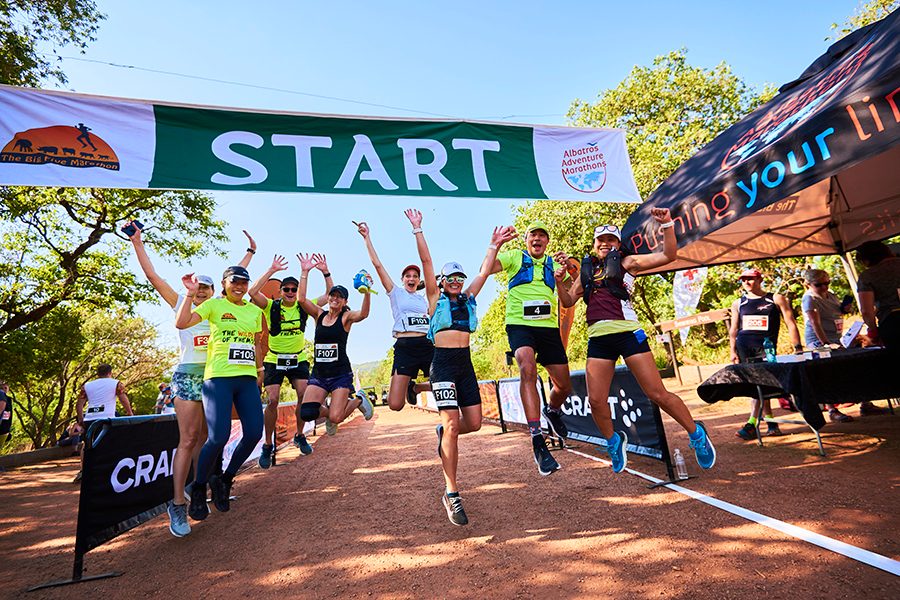 A group of Big Five Marathon runners cheering, jumping and laughing at the Entabeni Safari Conservancy in South Africa on a sunny day 