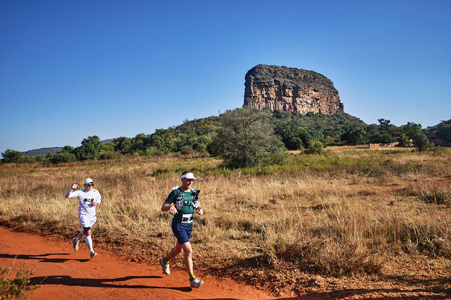 Two Big Five Marathon runners running across the Entabeni Safari Conservancy in South Africa on a sunny day