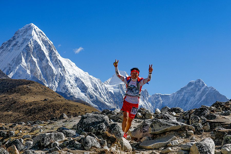 A man smiling and cheering while running down the rocky mountains at the Everest Base Camp on the Everest Marathon trail