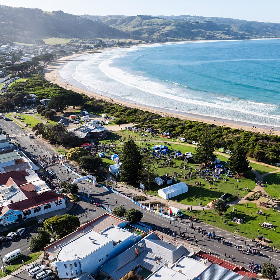 A bird’s eye view of runners running on the road for the Great Ocean Road Marathon on a sunny day with a view of the vast blue sea in the distance