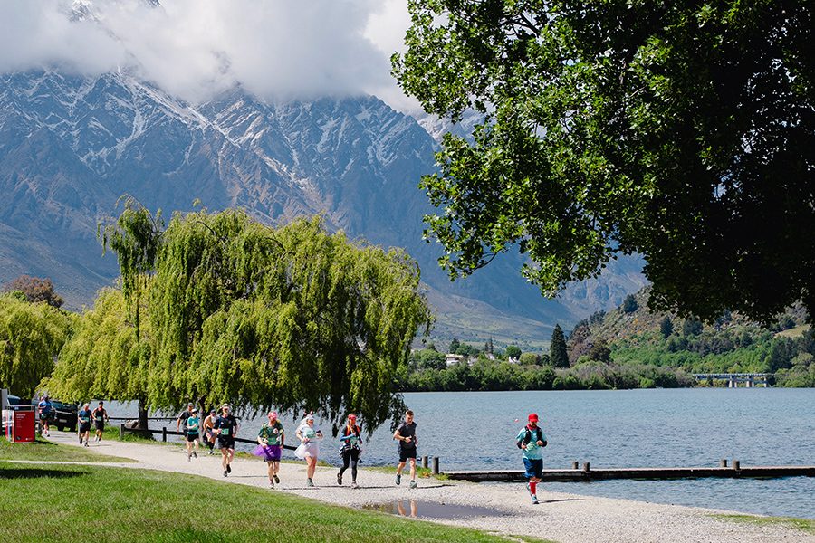 Runners on running on the Queenstown Marathon trail by the lake with views of a mountain in the background in New Zealand 