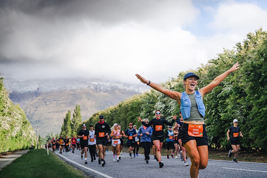 A woman cheering ahead of a crowd of Queenstown Marathon runners in New Zealand with a view of the forest and mountains in the background
