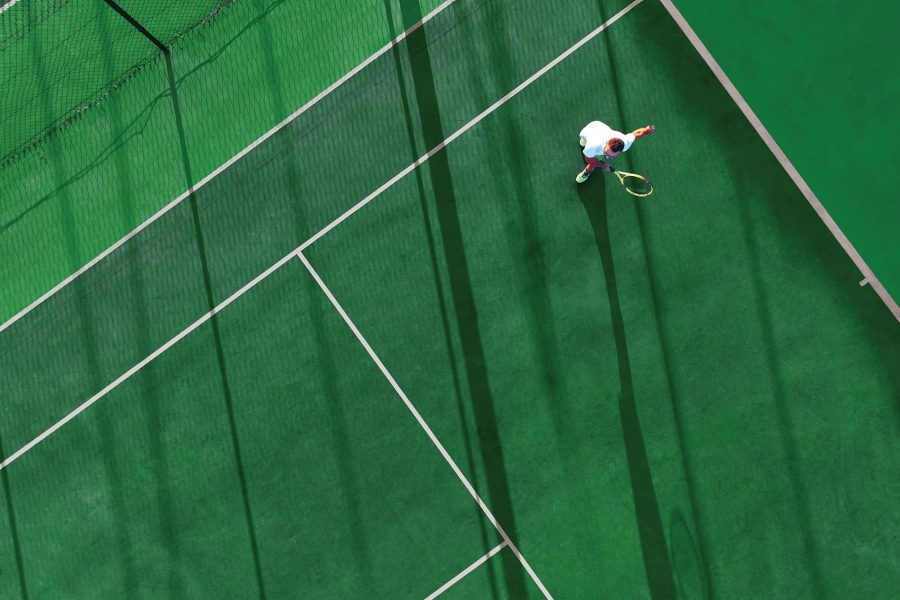 A drone shot of a man playing tennis on a green tennis court during daytime