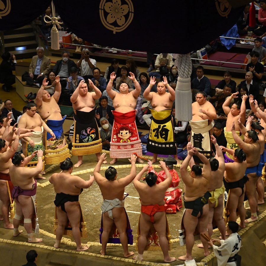 Sumo wrestlers standing in a circle while a crowd watches in Tokyo.