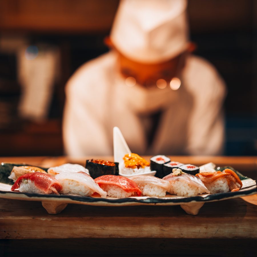 A closeup of a platter of sushi and the chef in the background at an omakase restaurant in Tokyo.