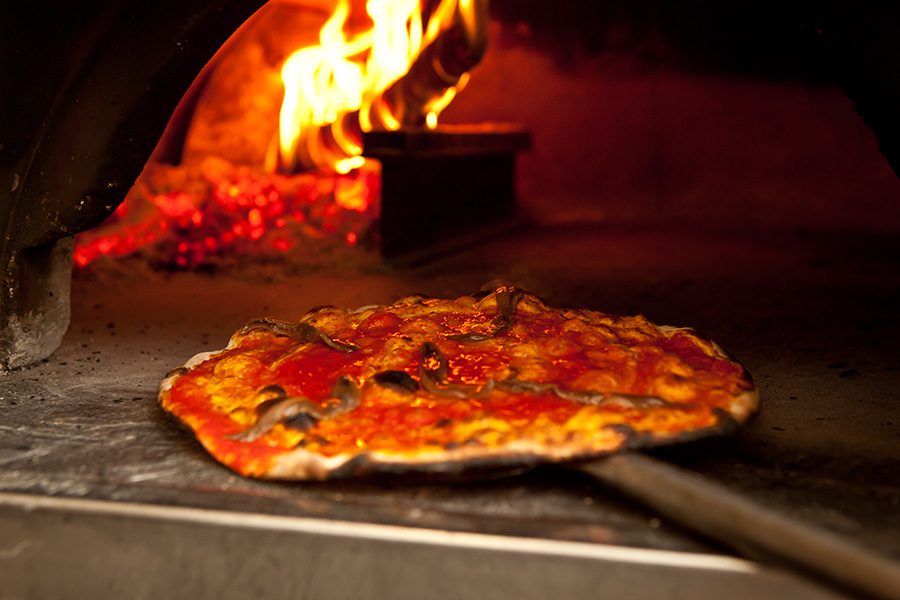 Pizza being placed in a wood-fired oven.