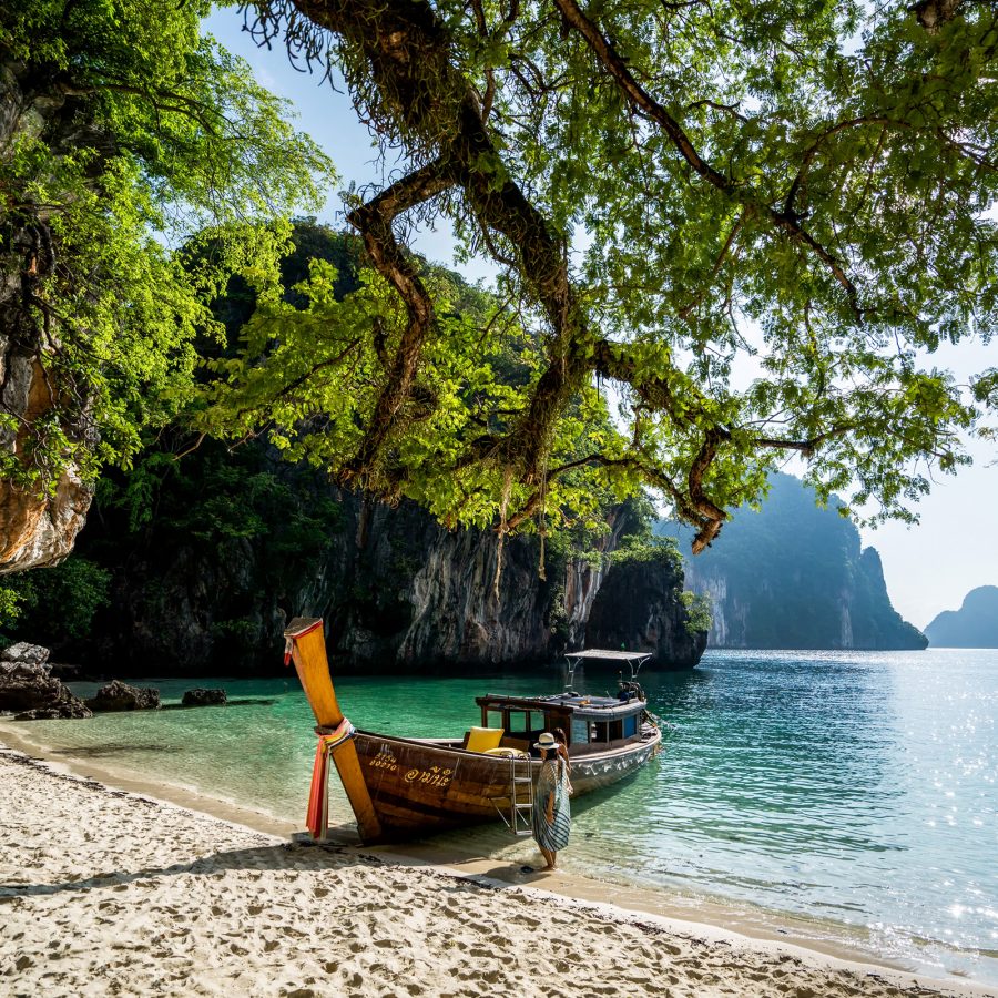 A woman standing by a boat moored at the beach at Six Senses Yao Noi, with other islands in the background. 