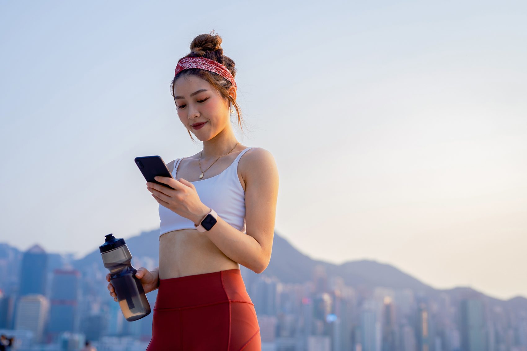Next to Hong Kong’s harbour, a woman on an evening jog, with a water bottle in hand, looks down and smiles at her phone. 